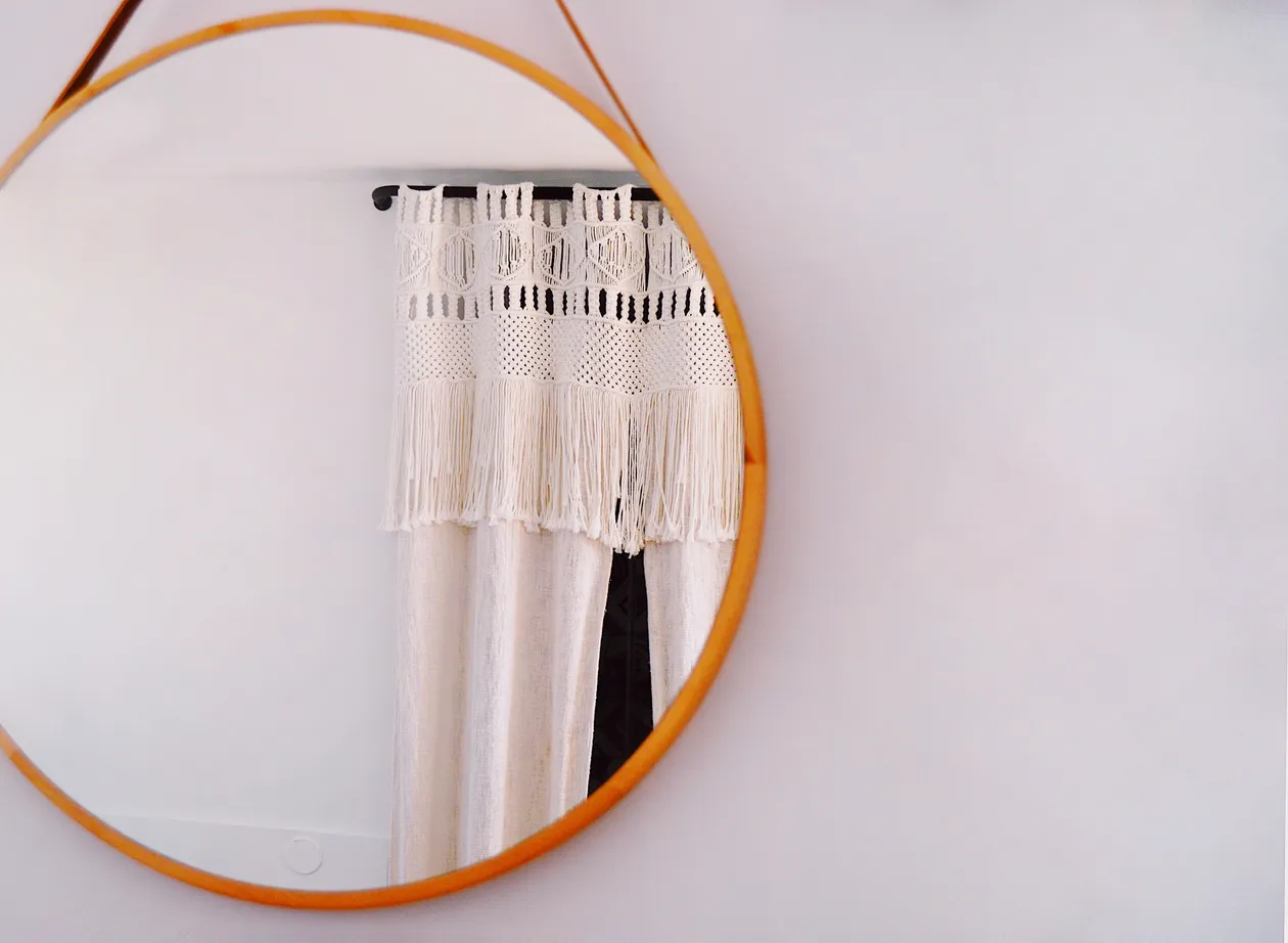 Round mirror reflecting a macrame wall hanging, used to correct an irregular home shape